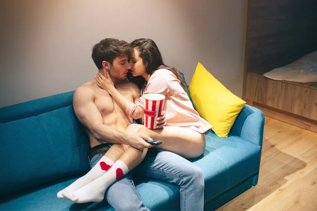 The girl kissing a boy on cough in a living room. 